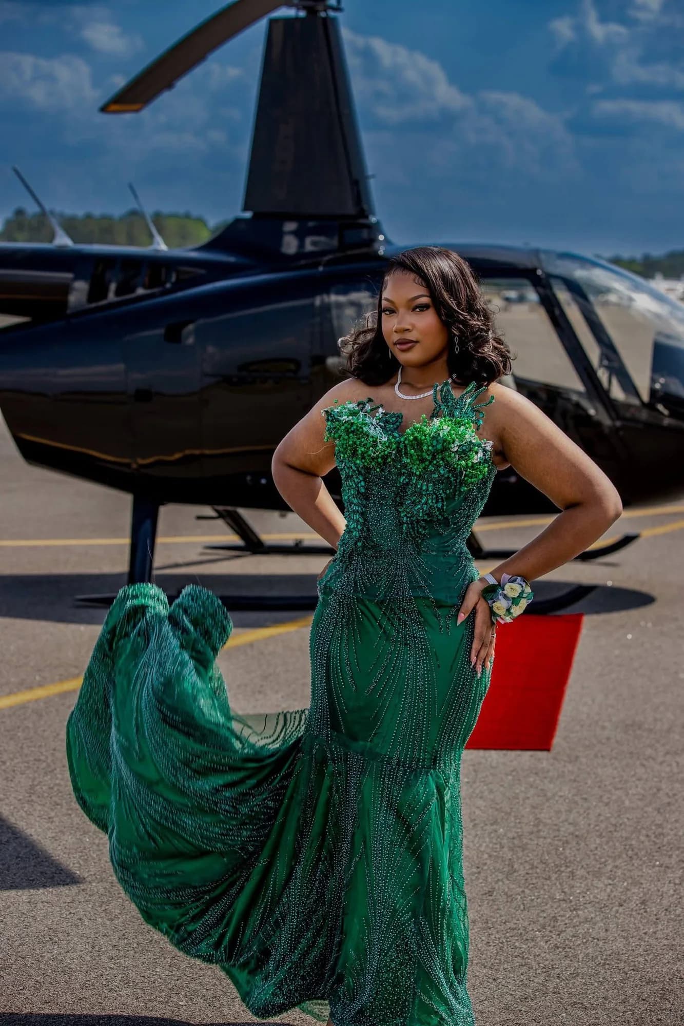 Client wearing an emerald beaded gown beside a helicopter