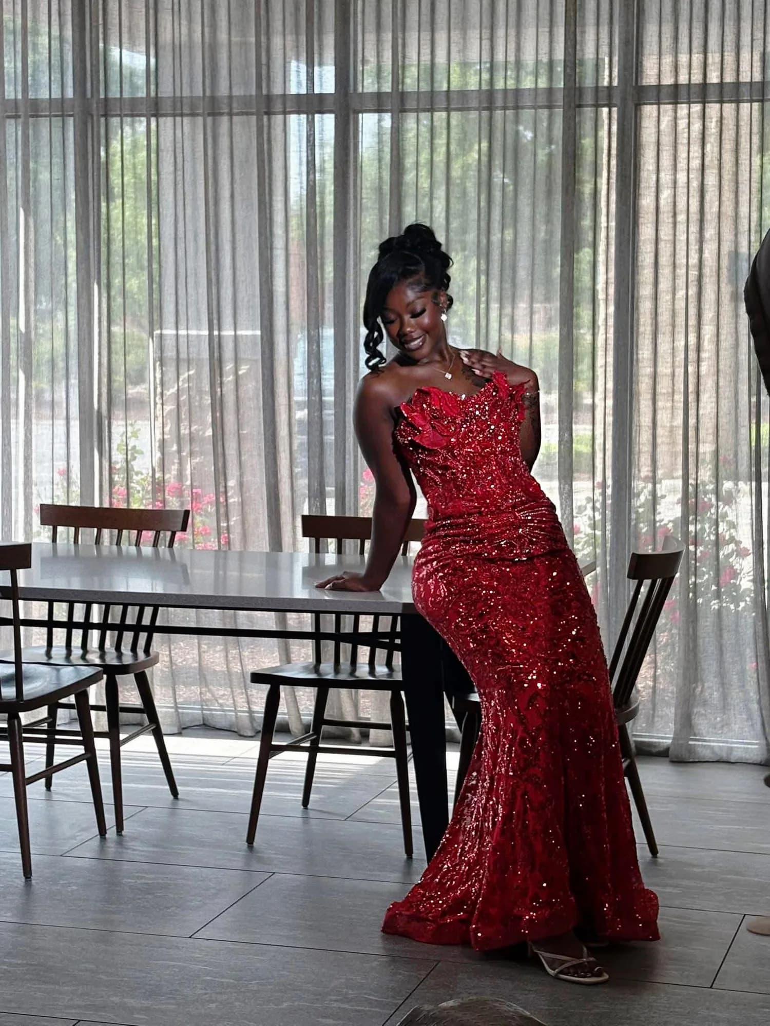 Client wearing a red sculptural sequin gown beside a wall of windows