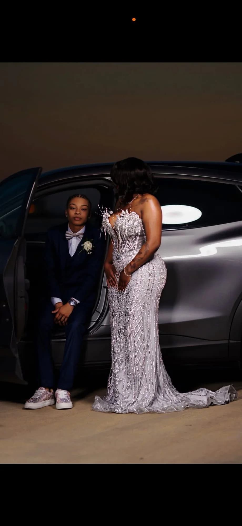 Client wearing a silver crystal evening gown beside a car